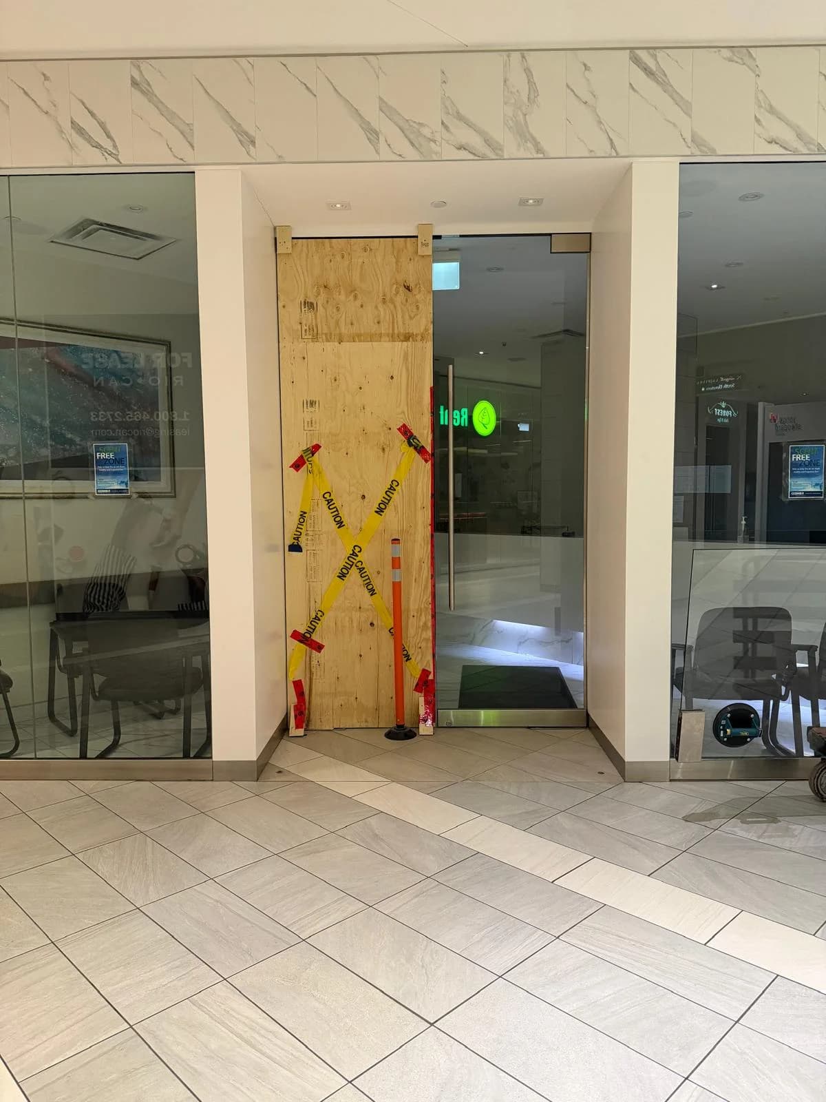 Commercial glass entrance with one door opening covered by plywood and caution tape before replacement