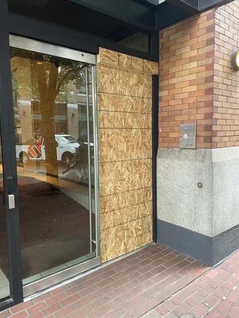 The same Vancouver entrance with the damaged glass opening covered by a temporary board-up and debris cleared