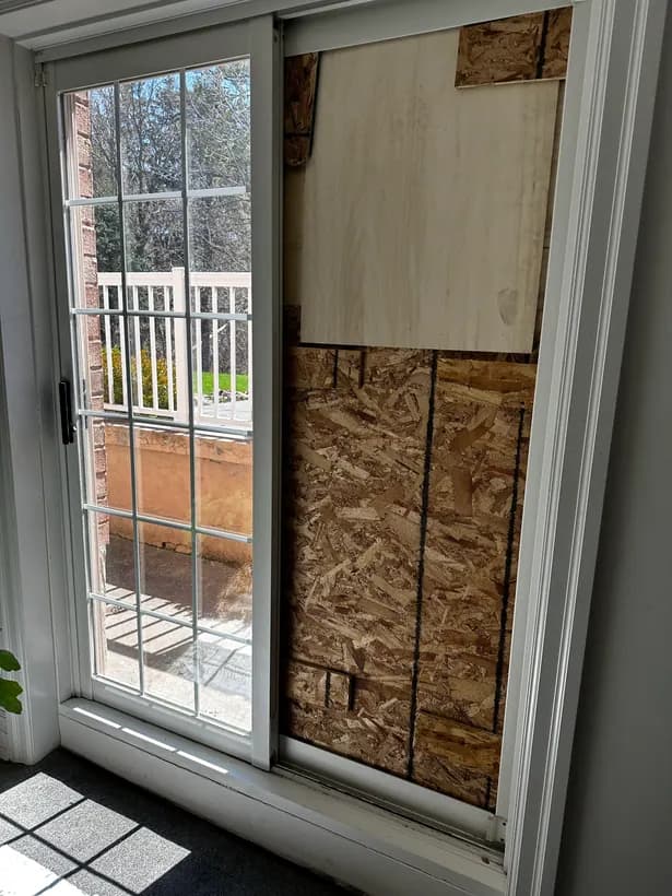 Residential patio-door opening temporarily secured with wood panels after damage